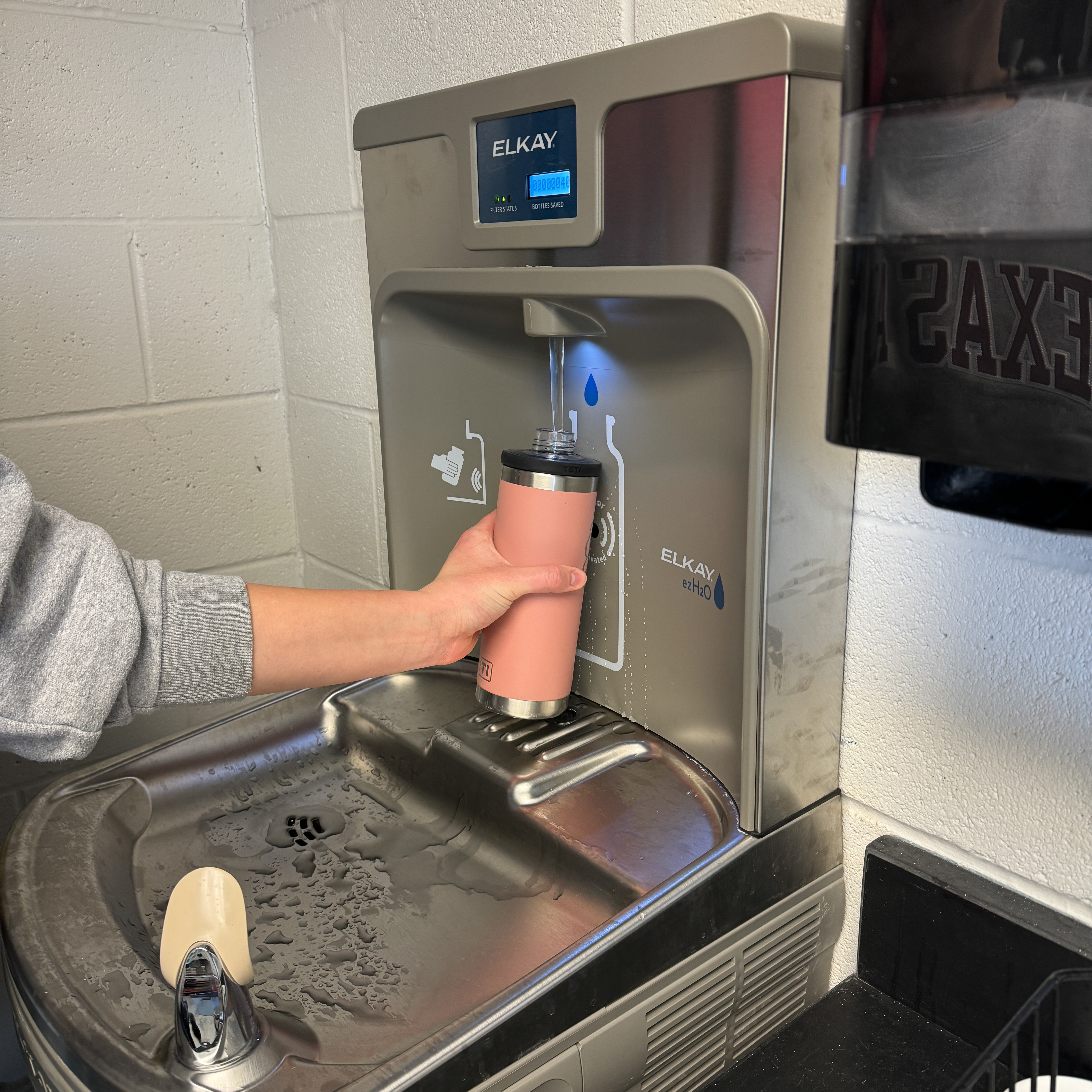 Water fountain with a user filling a reusable pink tumbler.